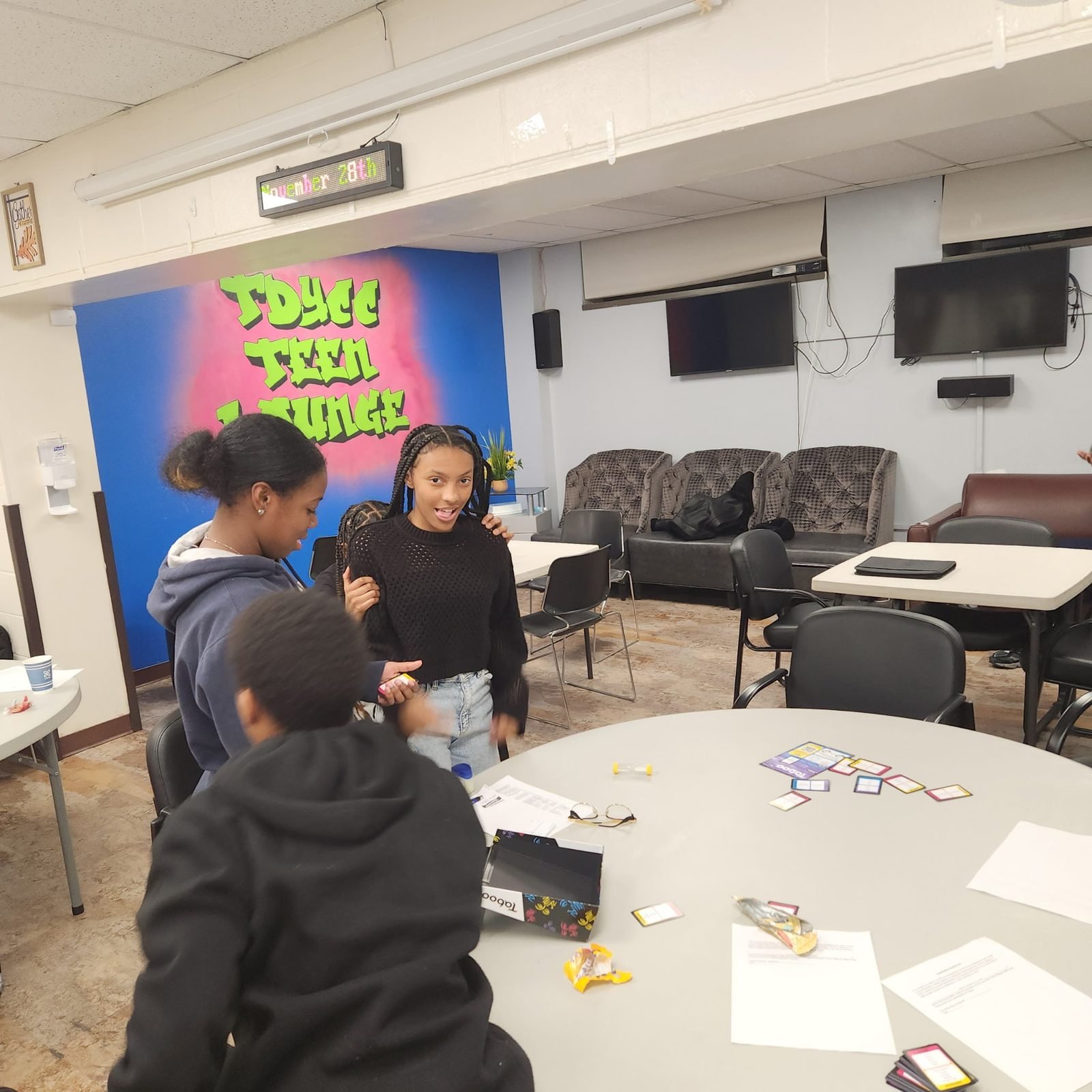 Youth playing a card game around a table in the Teen Lounge