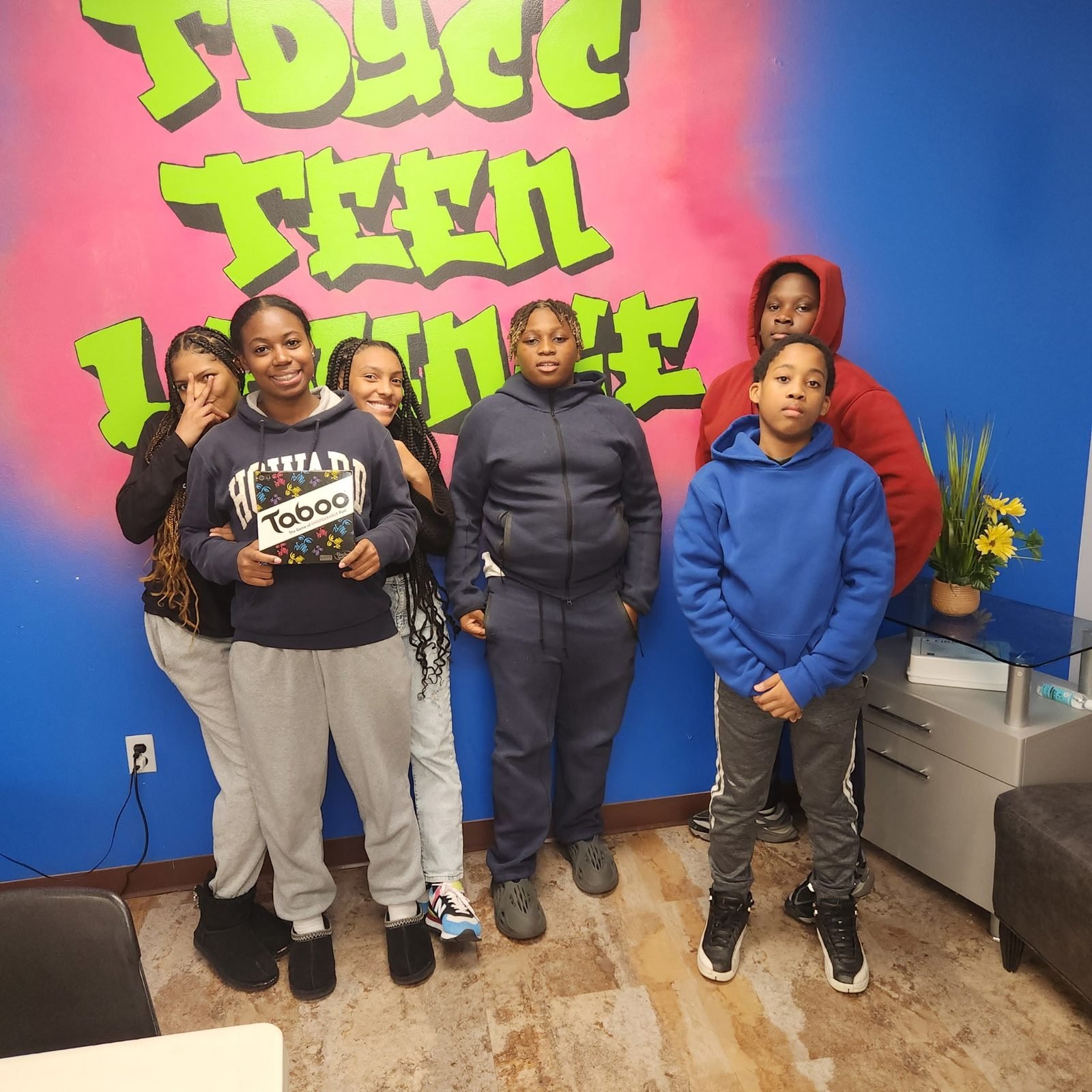 CCWW youth posing in front of a graffiti mural in the TDYCC Teen Lounge